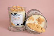 Candle with cookie-shaped wax pieces and visible label on a neutral background