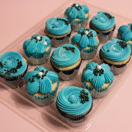 Blue frosted cupcakes with decorative elements on a clear plastic tray.